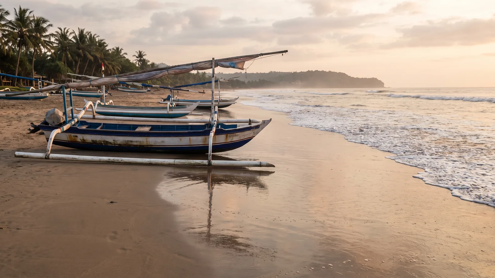 Traditionelle balinesische Auslegerboote aus Holz ruhen am weichen Sandstrand der Bucht von Jimbaran im warmen Abendlicht.