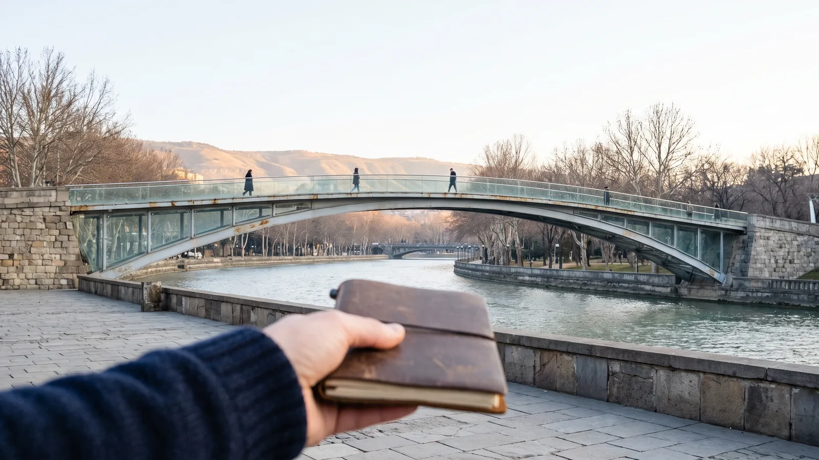 Die moderne Friedensbrücke aus Glas und Stahl spannt sich über den Fluss Kura im winterlichen Tiflis.