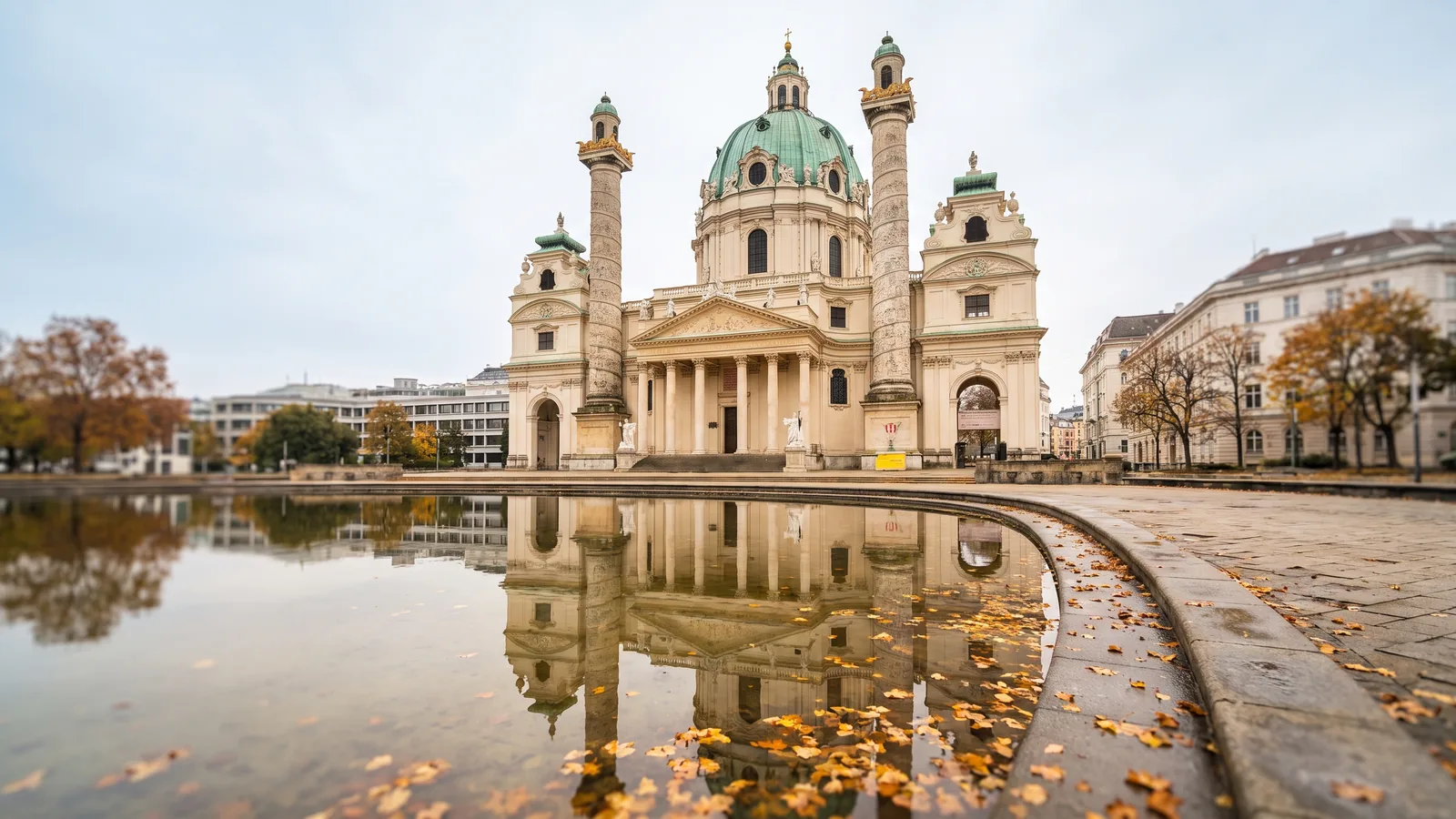 Karlskirche in Wien mit Barockfassade und grünem Kupferdach, gespiegelt im Wasserbecken an einem klaren Novembermorgen.