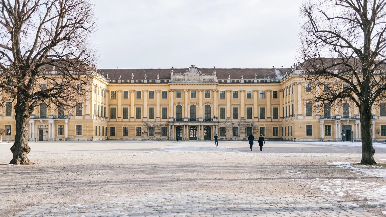 Die weitläufige barocke Fassade von Schloss Schönbrunn im kühlen Winterlicht mit dem großen Ehrenhof davor.