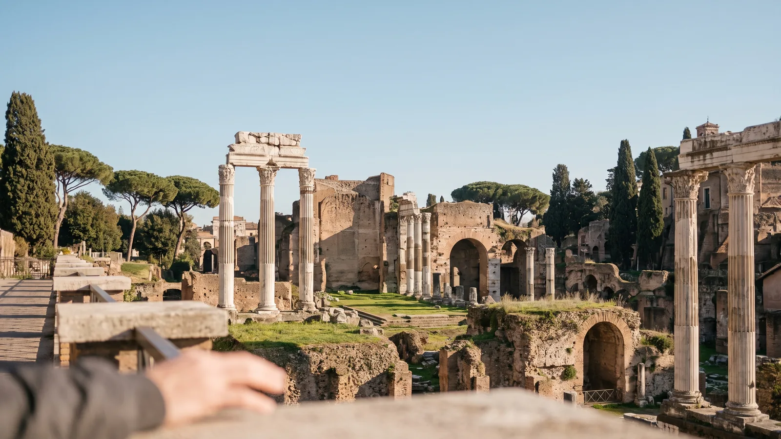 Blick über die antiken Säulen und Ruinen des Forum Romanum unter zartem Frühlingshimmel mit Zypressen.