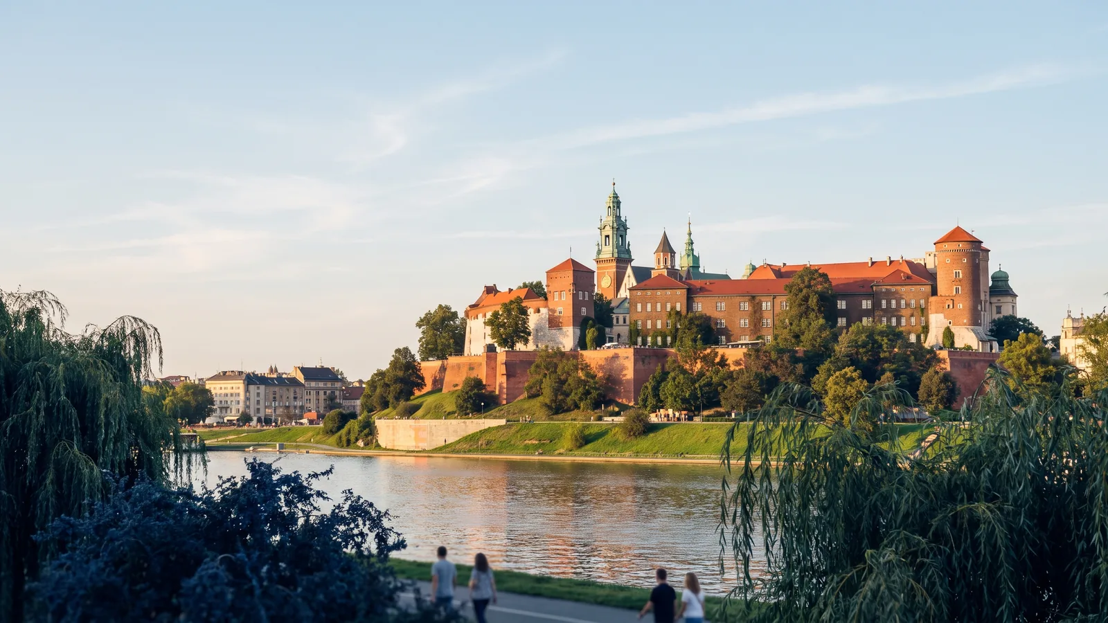 Blick über die ruhige Weichsel auf die historische Wawel Burg im warmen Licht eines Sommertags in Krakau.