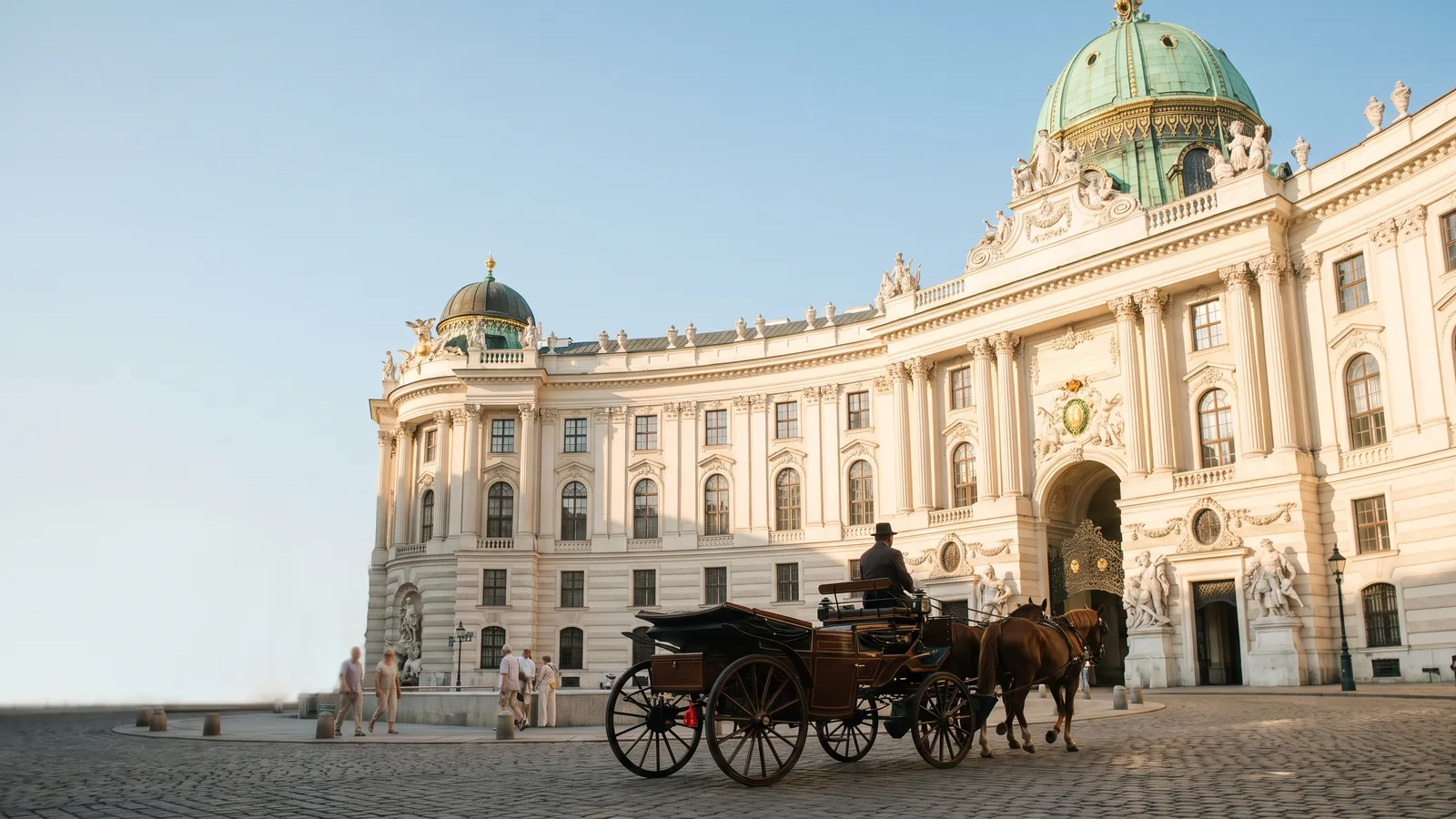 Der prachtvolle Michaelertrakt der Wiener Hofburg an einem sonnigen Sommertag mit einer Kutsche auf dem Kopfsteinpflaster.