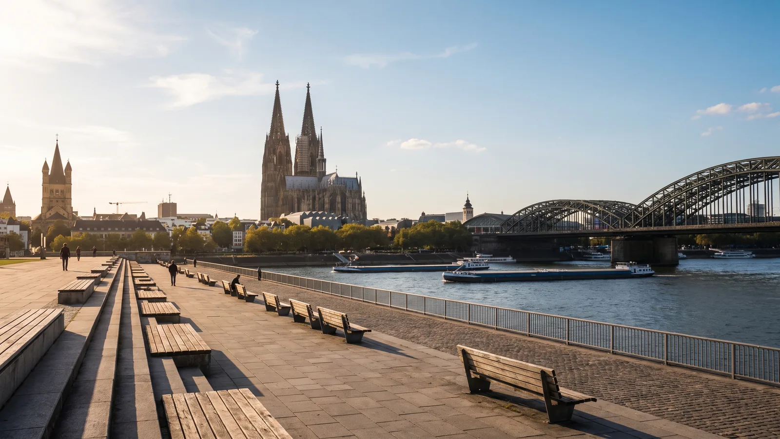 Blick vom Deutzer Rheinufer auf den Kölner Dom und die stählerne Hohenzollernbrücke im goldenen Nachmittagslicht.