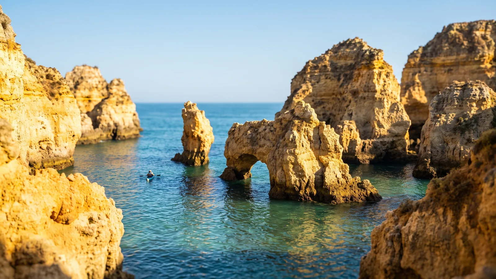 Goldgelbe Felsklippen und natürliche Steinbögen im türkisfarbenen Wasser der Algarve unter strahlend blauem Sommerhimmel.