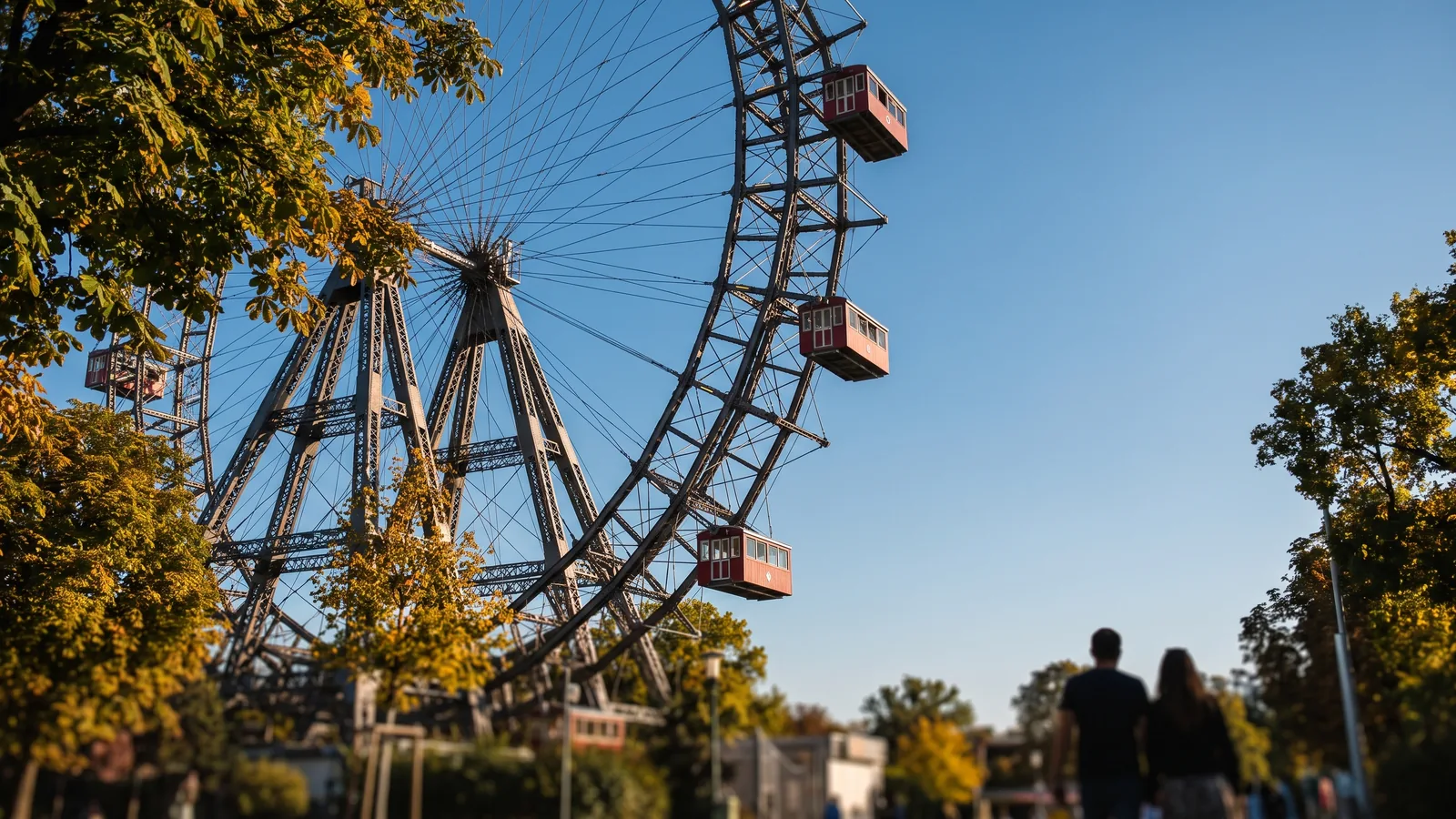 Das historische Wiener Riesenrad mit roten Waggons im grünen Prater unter spätsommerlichem blauem Himmel.