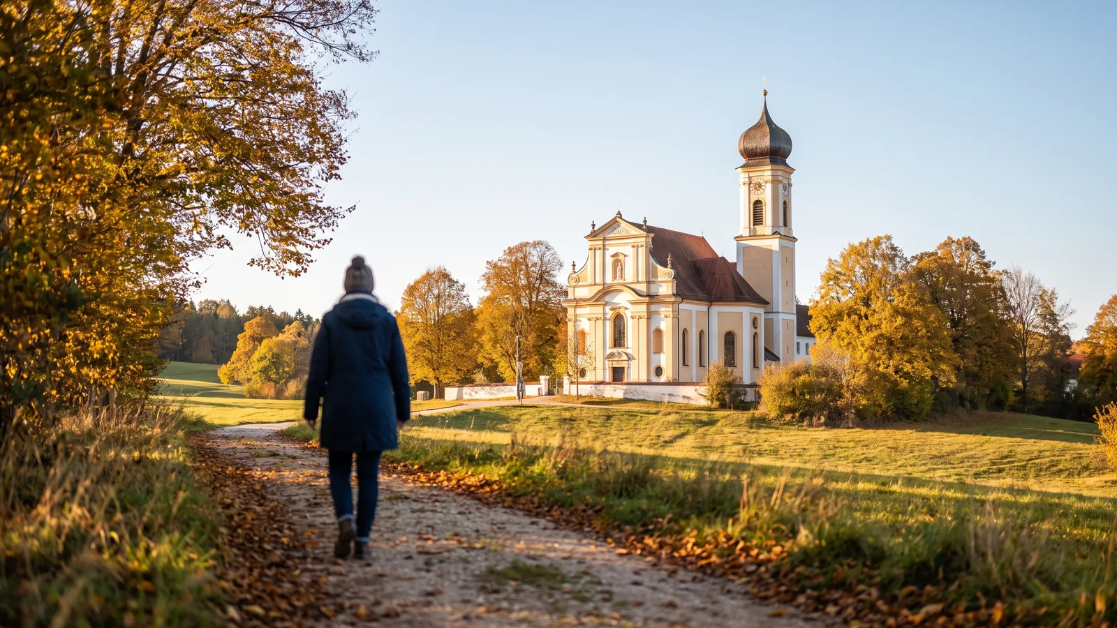 Blick auf die barocke Asambasilika in Altenmarkt bei Osterhofen hinter herbstlich gefärbten Bäumen im goldenen Nachmittagslicht.