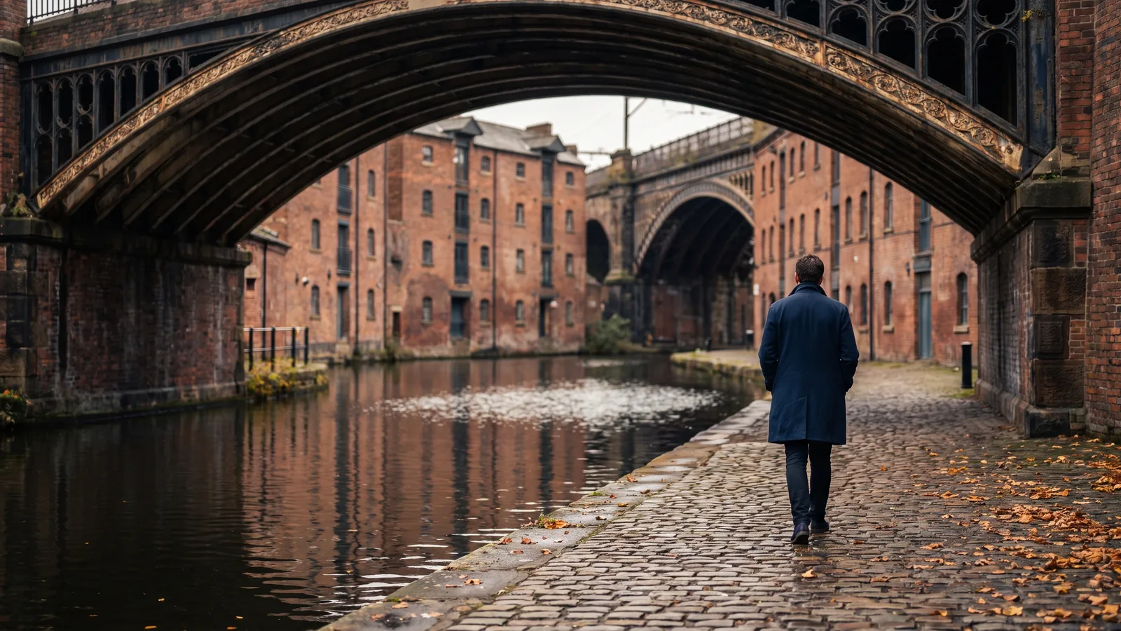 Historische Backsteinviadukte und ein Kanalbecken mit kopfsteingepflastertem Uferweg im herbstlichen Castlefield in Manchester.