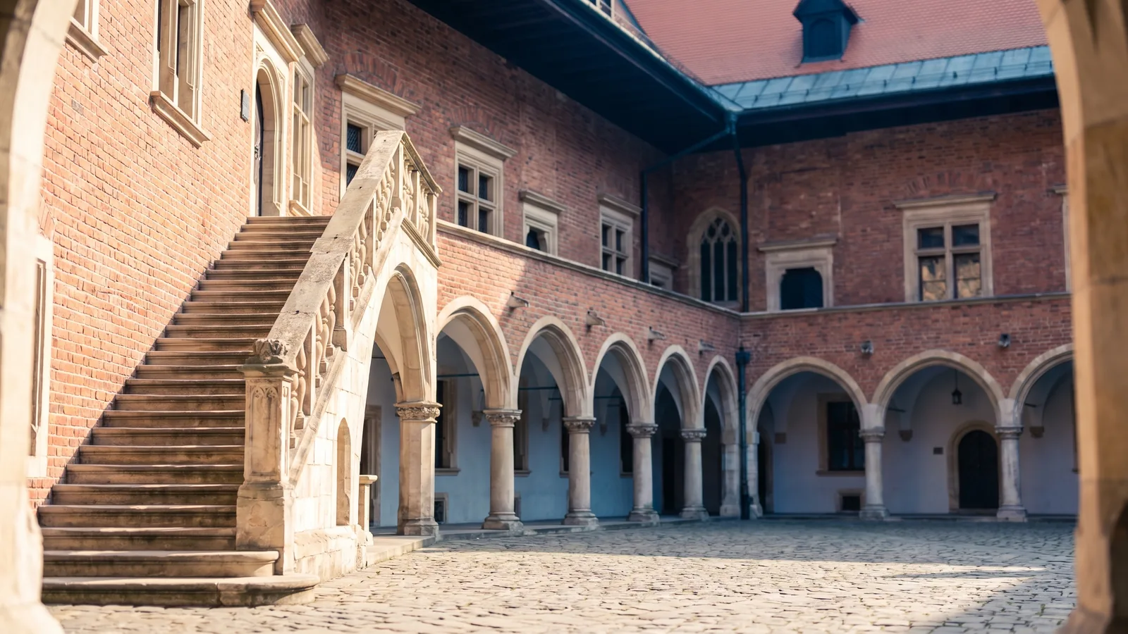 Der gotische Innenhof des Collegium Maius in Krakau mit roten Backsteinarkaden und historischer Steintreppe im Frühlingslicht.