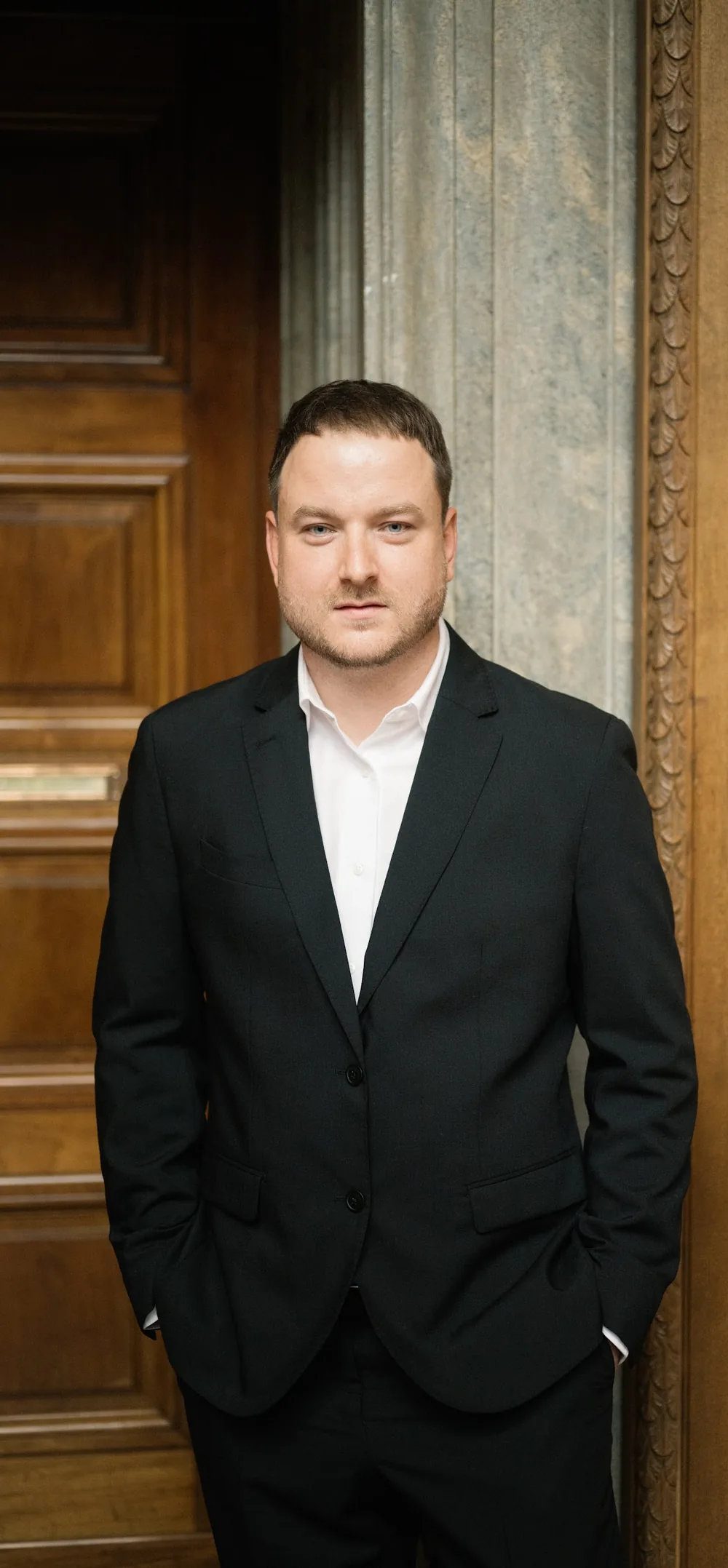 Florian Hartl im dunklen Anzug vor einer Holztür